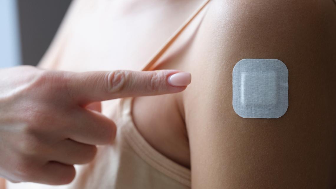 Woman showing her finger plaster under injection site of coronavirus vaccine closeup. 