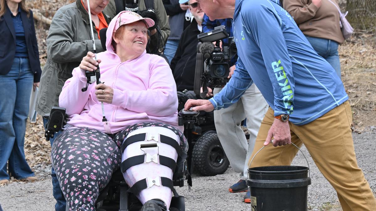 Minnesota Gov. Tim Walz, right, asks Jennifer Skiff, of Lonsdale, Minnesota, not to catch all the rainbow trout he is about to release into a restored Browns Creek in Stillwater on Friday, May 8, 2026. Skiff, who is a member of Capable Partners, an organization that helps people with physical challenges access outdoor activities, was fishing from an accessible fishing platform. As part of the Minnesota Governor's Fishing Opener in Stillwater, the Minnesota Department of Natural Resources is stocking trout in the creek. (John Autey/Pioneer Press/TNS)