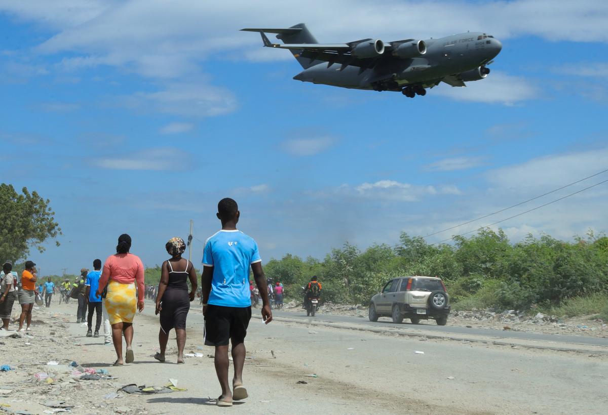 Residents walk along a street while fleeing their homes in Cite Soleil after rival gang clashes in Haiti's capital worsened over the weekend, as a U.S. Air Force Boeing C-17A Globemaster III aircraft (08-8204) prepares to land at Toussaint Louverture International Airport in Port-au-Prince, Haiti, May 11, 2026. REUTERS/Fildor Pq Egeder