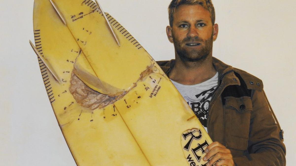 Shannon Ainslie and the board with a bite in it. (Chicco Mattos via SWNS). 
