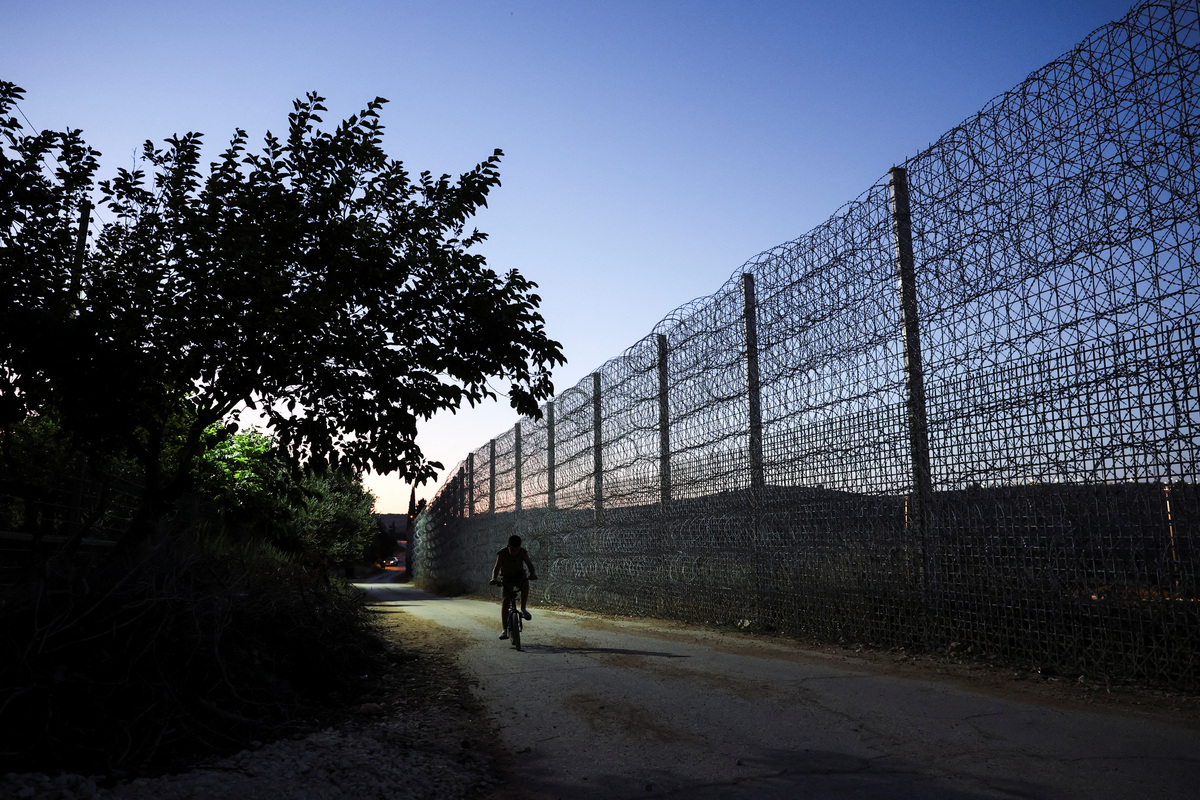 Yousef Foqahaa cycles past the tall metal fencing installed by the Israeli military that closed off four of the five entrances to his town, Sinjil, near Ramallah, in the Israeli-occupied West Bank, June 26, 2026. REUTERS/Ammar Awad