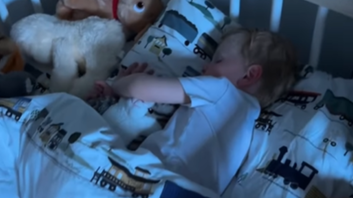 A 3-year-old toddler boy napping in his bed. 