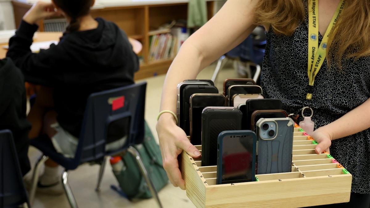 A Chicago teacher carries a box filled with students' cellphones in a classroom in March 2025.
