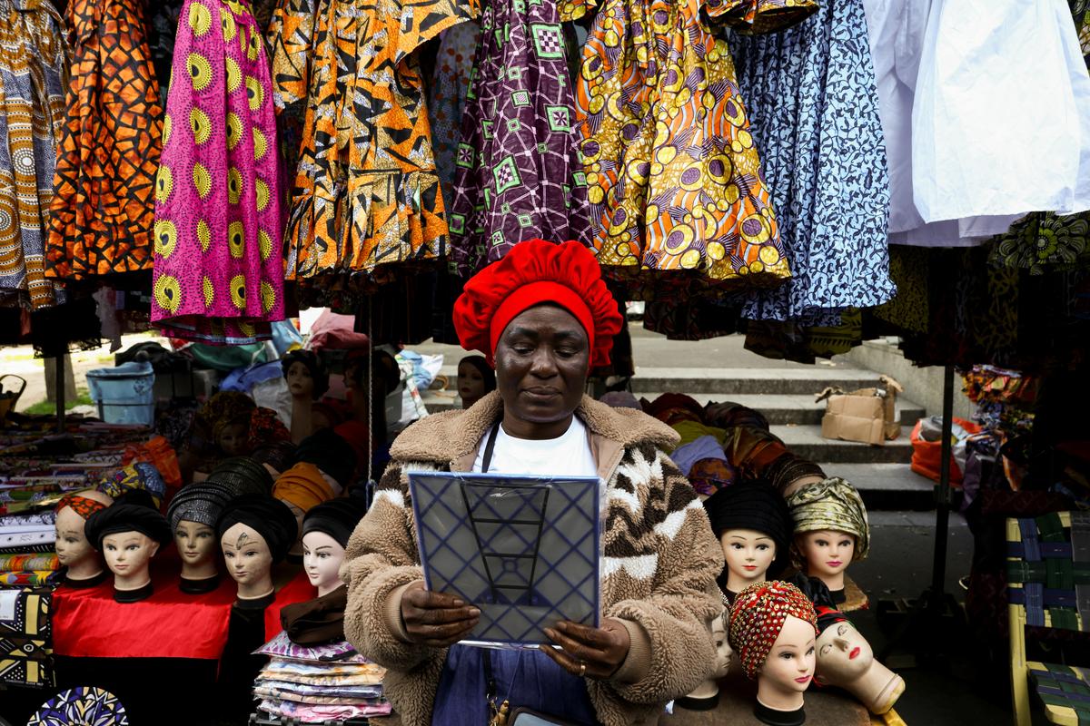 A woman tries on a new hat in the 800 metre-long Tuesday Market in Sarcelles, which has vendors selling food, clothing, homeware products and handicrafts to cater for Sarcelles' diverse immigrant community in the Paris suburb of Sarcelles, France, April 14, 2026. REUTERS/Tom Nicholson