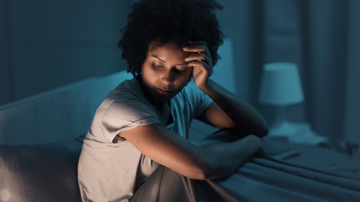 Sleepless african american woman sitting in bed at night, she is stressed and unable to sleep