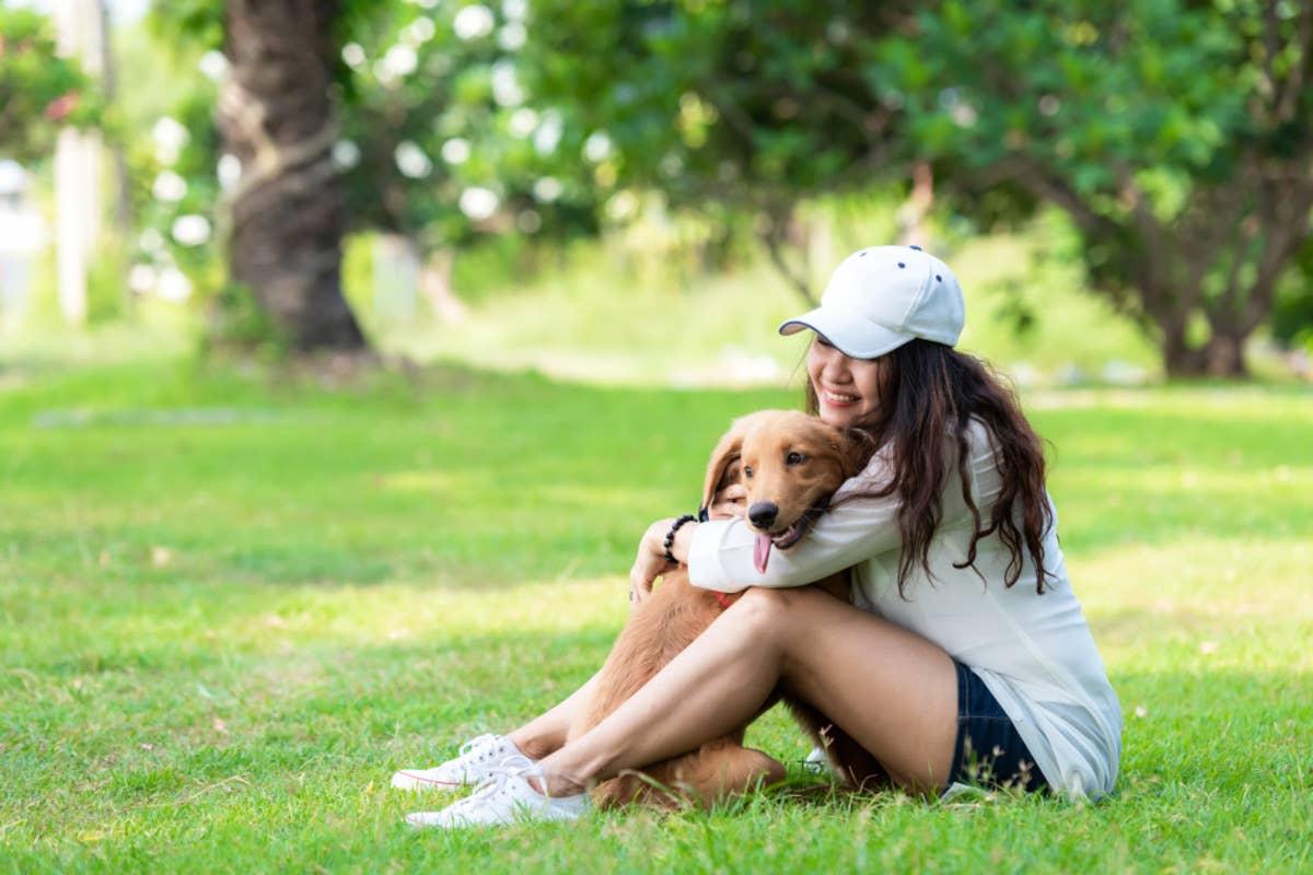 Woman sitting in the grass hugging her dog.