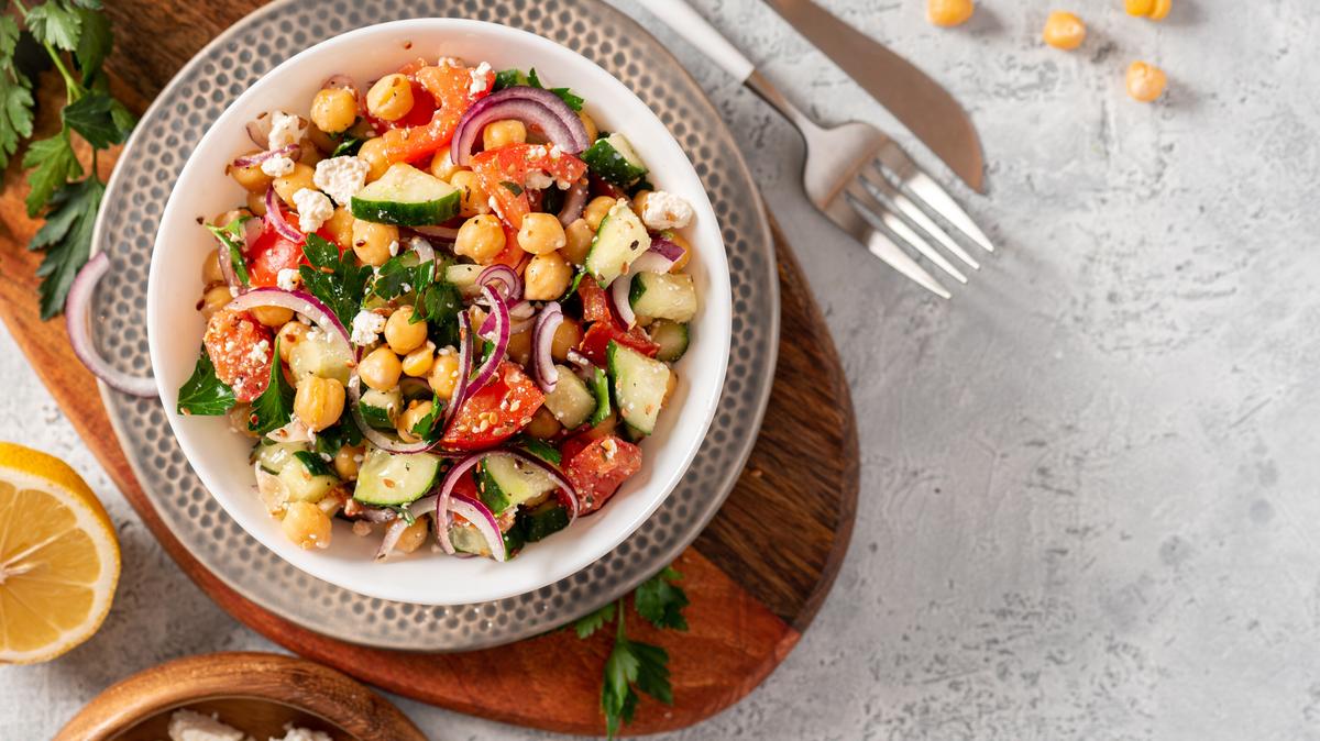 Chickpea salad with tomatoes, cucumber, feta cheese, parsley, onions and lemon in a plate on a gray background top view, selective focus. Healthy vegetarian food, oriental and Mediterranean cuisine.