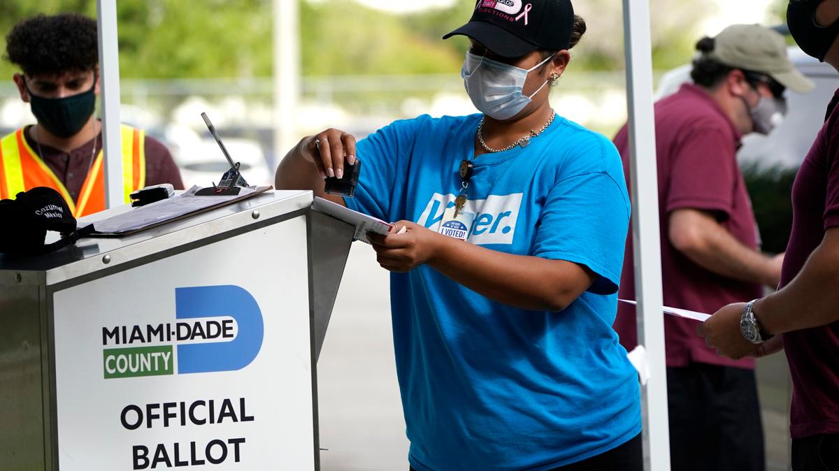 In October 2020, an election worker stamps a vote-by-mail ballot dropped off by a voter before placing it in an official ballot drop box at the Miami-Dade County Board of Elections in Doral, Fla.