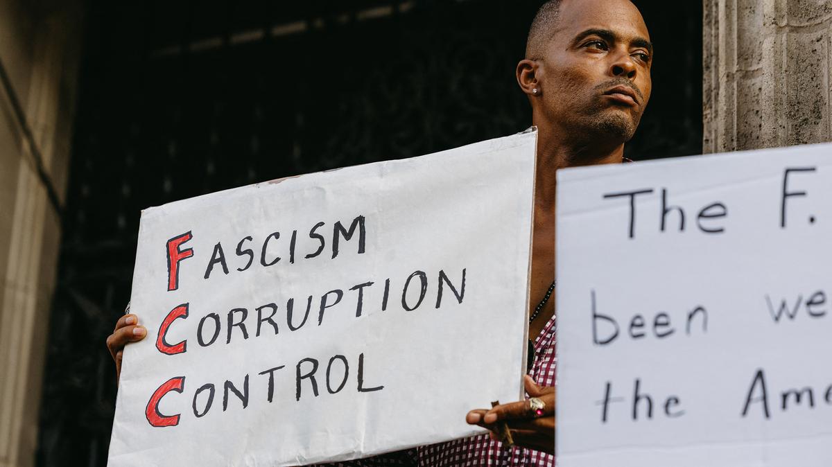 A demonstrator holds a sign reading "FCC: Fascism Corruption Control" outside the El Capitan Theatre on Hollywood Boulevard in Hollywood, California, on Thursday, Sept. 18, 2025. The taping of "Jimmy Kimmel Live!" was suspended earlier in the day, leading people to gather at the venue with protest signs. (David Pashaee/Middle East Images via AFP/Getty Images/TNS)