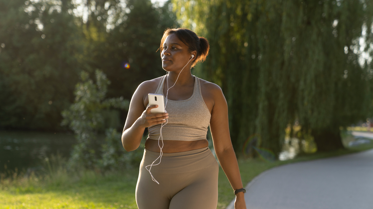 Plus sized African American woman using her mobile phone and earphones during a walk at the park on a summer day. 