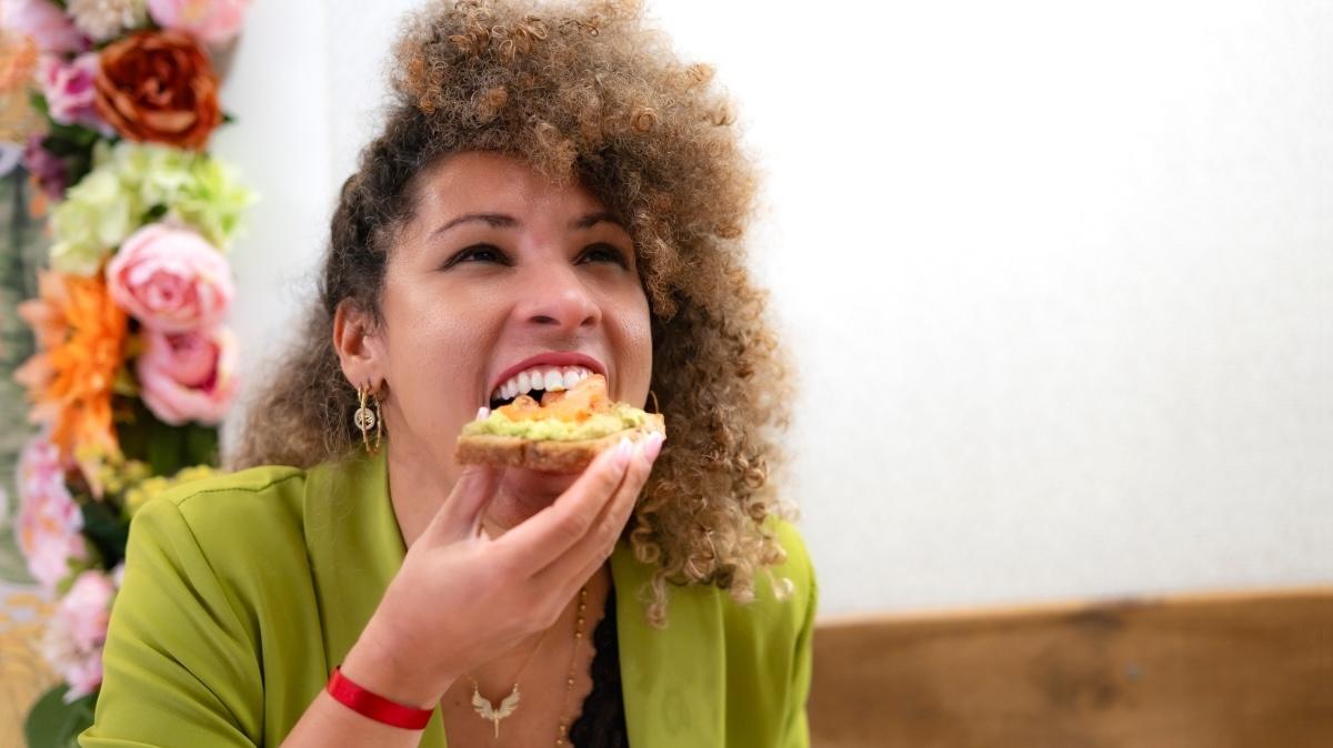 Curly haired female entrepreneur enjoying a healthy snack of avocado toast in a stylish cafe