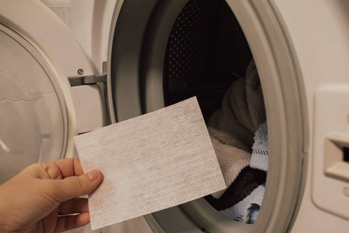  A hand holding a dryer sheet by the washing machine.