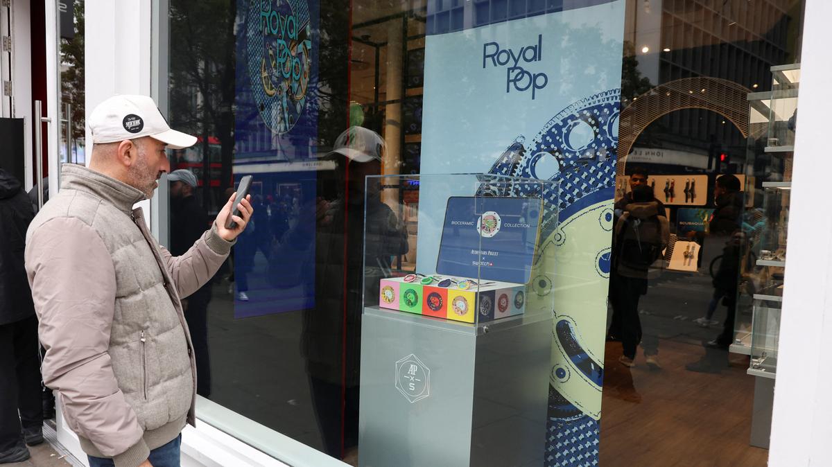 A man talks to someone on video call, while looking at an Audemars Piguet and Swatch "Royal Pop" watches in a box at a Swatch shop in London, Britain, May 18, 2026. REUTERS/Corey Rudy