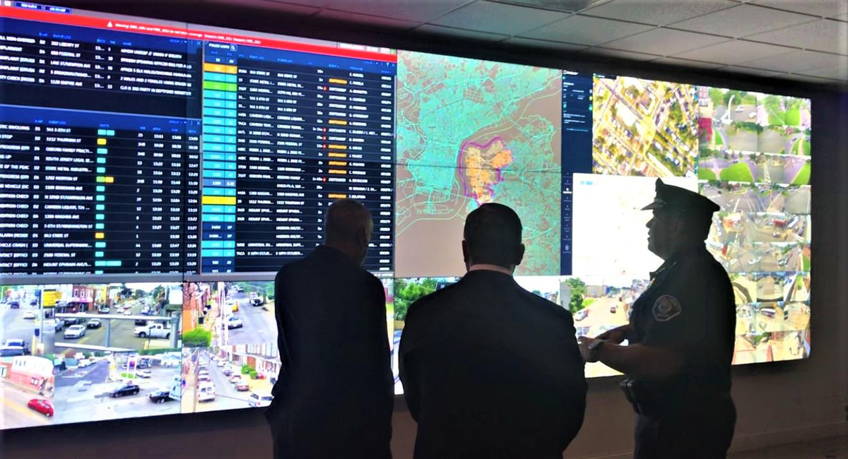 Camden Mayor Victor Carstarphen, left, and N.J. Assemblyman William Moen, center, listen to county Police Chief Gabriel Rodriguez explain monitors during a tour July 31, 2023, of the Real Time Tactical Information Center on Federal Street. Displays variously track officers on assignment, camera feeds, and gunshot reports from the ShotSpotter network.