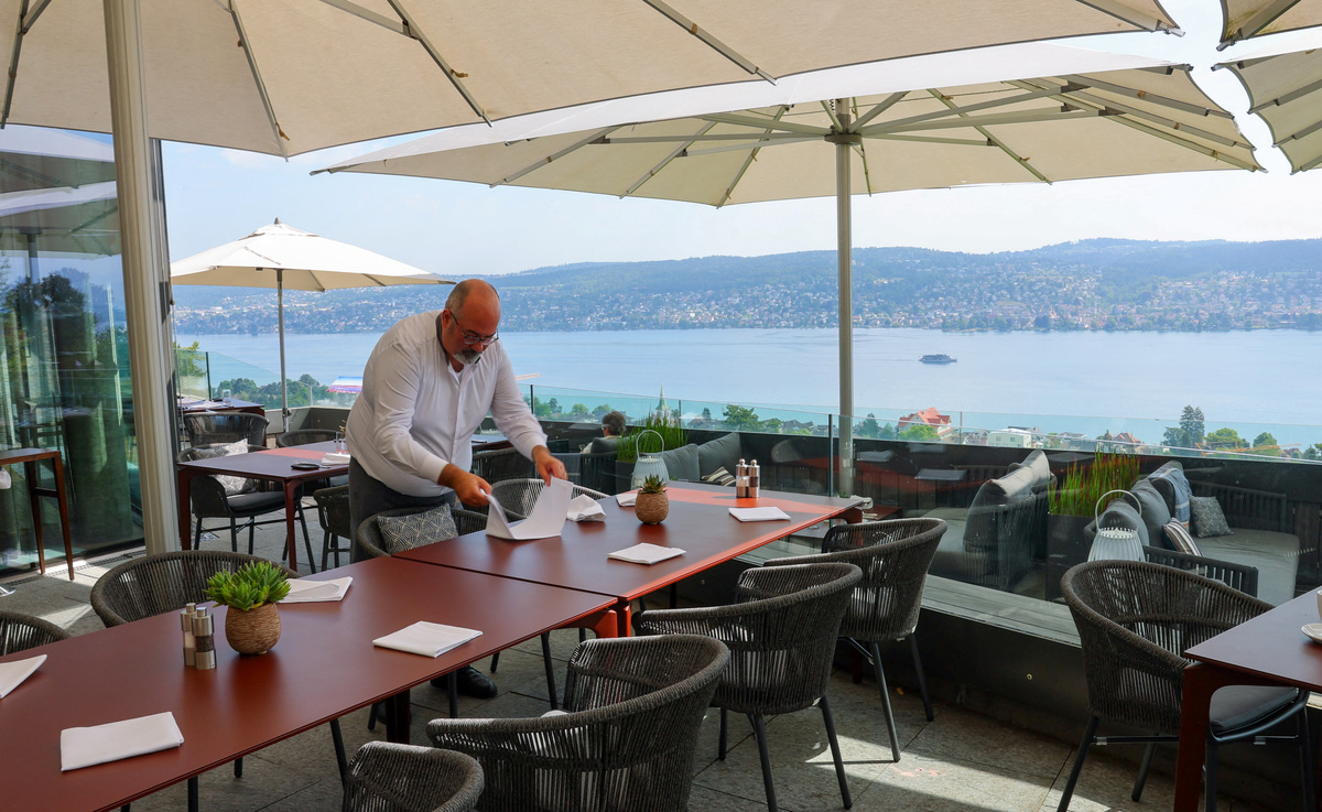 A Hotel Belvoir staff member sets a table on a terrace overlooking Lake Zurich, ahead of a June 14 vote on a plan backed by the right‑wing party to limit population growth to 10 million inhabitants, in Ruschlikon, Switzerland, May 27, 2026. REUTERS/Denis Balibouse