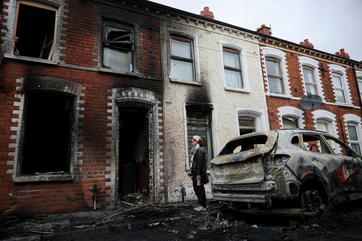 A resident looks at the charred debris scattered on the street in her neighbourhood, in the aftermath of anti-immigrant protests following a knife attack on June 8, which left a man seriously injured and prompted police to declare a critical incident, at Lendrick street, east Belfast, Northern Ireland, June 10, 2026. REUTERS/Isabel Infantes