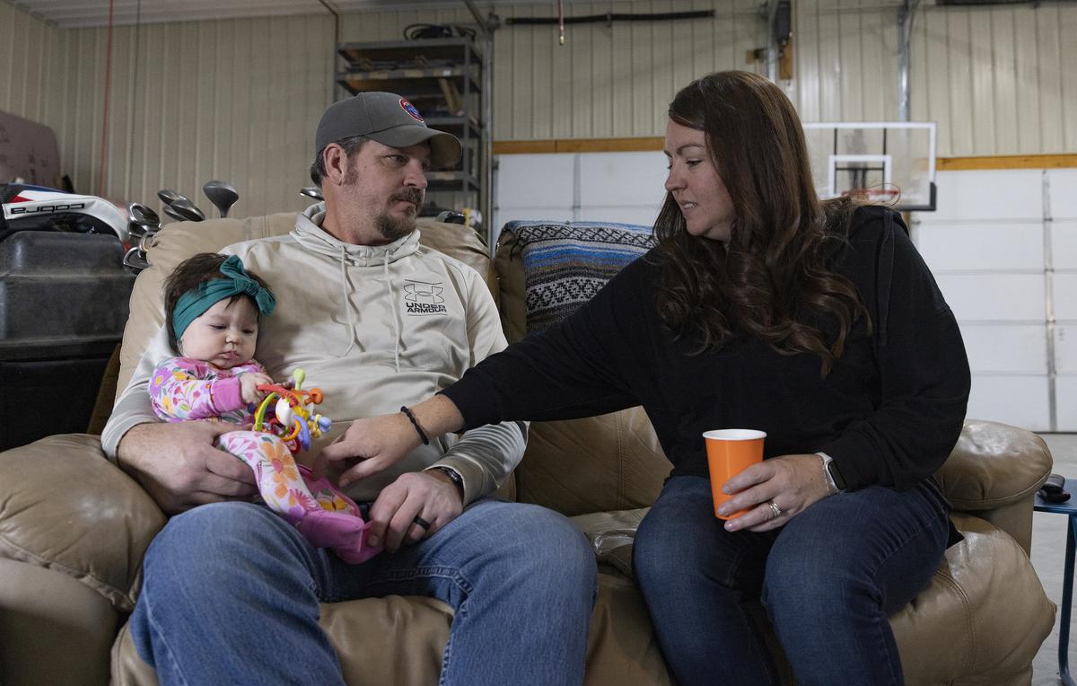 Rickey Malloy with his wife Jenny, and their four-month-old granddaughter Adaline, at home in Hillsboro, Ill., on Feb. 1, 2026. The drug, tofersen, made by Biogen and marketed as Qalsody, is for a small subset of patients. But evidence that breathing and strength can get better for some of them is remarkable for a paralyzing, usually fatal disease. (Julia Rendleman/The New York Times)