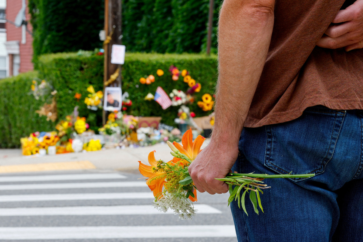 A person holds flowers while standing across the street from a makeshift street side memorial, a day after a U.S. Immigration and Customs Enforcement (ICE) agents fatally shot a driver, in Biddeford, Maine, U.S., July 14, 2026.  REUTERS/CJ Gunther