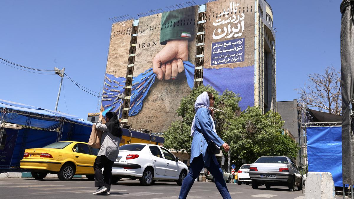 People cross a street near a billboard on the facade of a building depicting the Strait of Hormuz with a caption in Persian reading "Forever in Iran's Hand," at Vanak Square in Tehran, Iran, on Monday, May 25, 2026. (Atta Kenare/AFP/Getty Images/TNS)