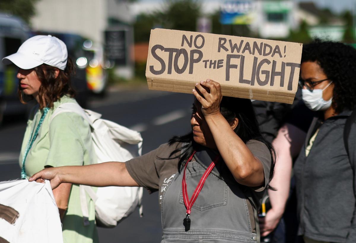 FILE PHOTO: An activist blocking a road leading away from the Colnbrook Immigration Removal Centre holds a banner during a protest against the British Governments plans to deport asylum seekers to Rwanda, near Heathrow airport in London, June 14, 2022. REUTERS/Henry Nicholls/File Photo