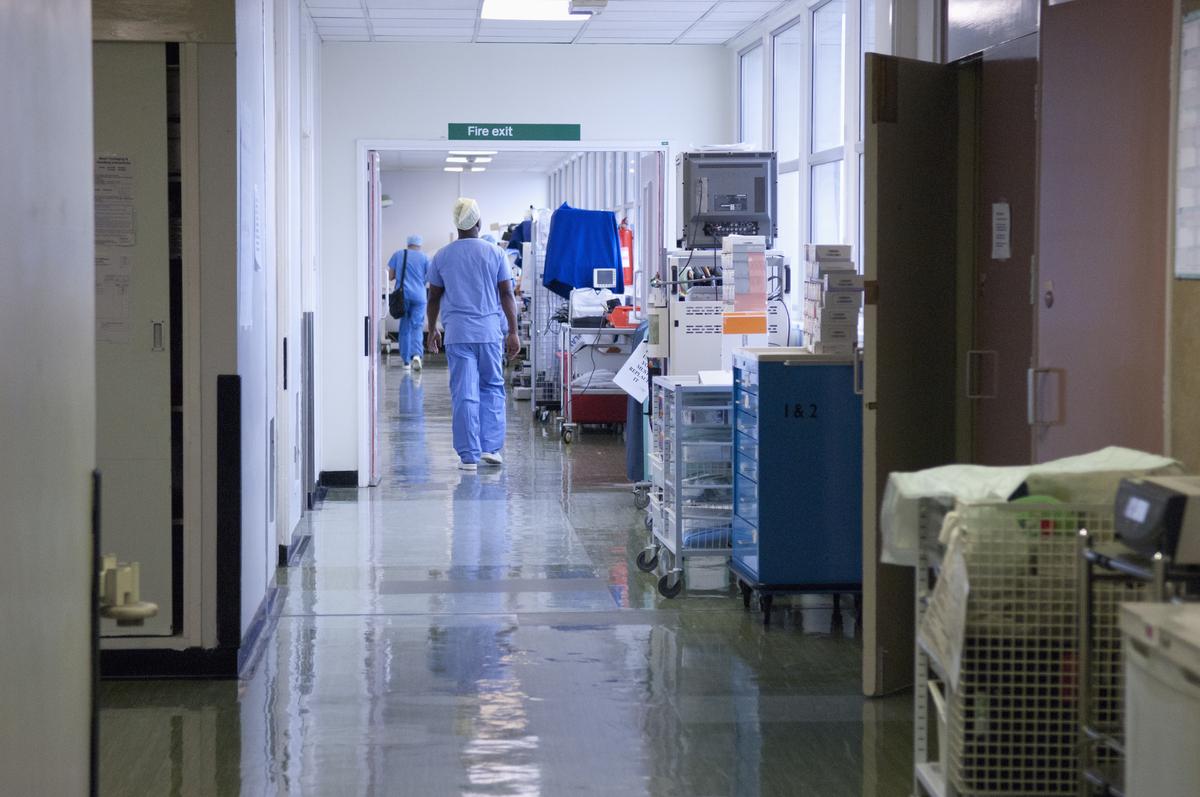  File: A health care worker walks down a hospital corridor toward a fire exit. 