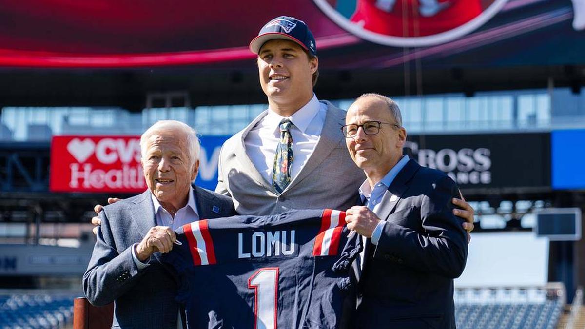  May 7, 2026; Foxborough, MA, USA; New England Patriots first round draft pick Caleb Lomu is presented with a ceremonial first round jersey by team owner Robert Kraft (l) and team president Jonathan Kraft (r) at a press conference on the game field at Gillette Stadium. Mandatory Credit: Natalie Reid-Imagn Images | Natalie Reid-Imagn Images 