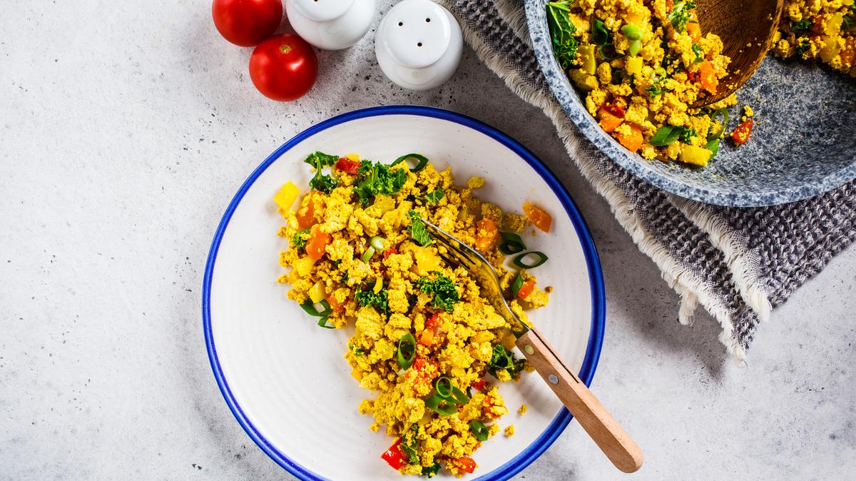 Tofu scramble with vegetables in white plate. Vegan Alternative food concept.
