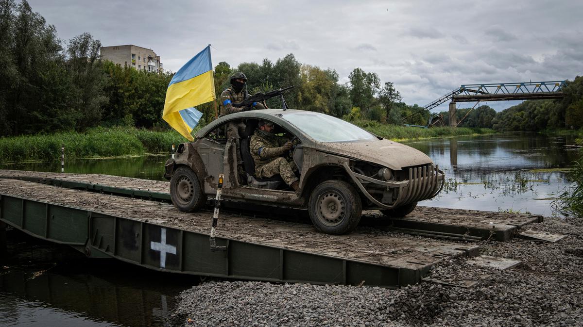 Paracaidistas ucranianos cruzan un puente militar sobre el río Siverskiy-Donets en un auto con una bandera ucraniana, en Izium, una zona ucraniana recién recuperada a las tropas rusas, el 14 de septiembre de 2022. (AP Foto/Evgeniy Maloletka)