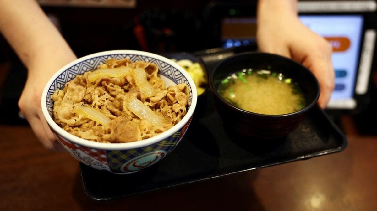 A staff member serves Japanese fast-food 'gyudon' beef bowl with miso soup inside Yoshinoya restaurant in Tokyo, Japan May 19, 2025.  REUTERS/Issei Kato