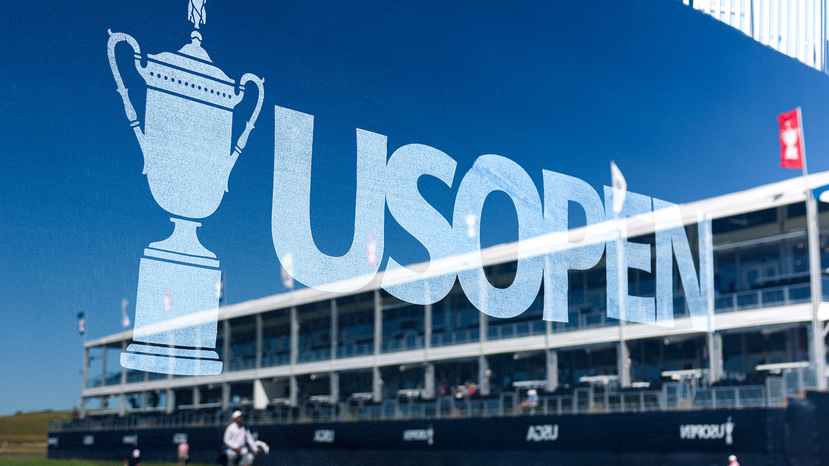 Jun 15, 2026; Southampton, New York, USA; The grandstand on hole 17 is seen through a reflection on glass in front of a US Open graphic during a practice round for the U.S. Open golf tournament. Mandatory Credit: Bill Streicher-Imagn Images