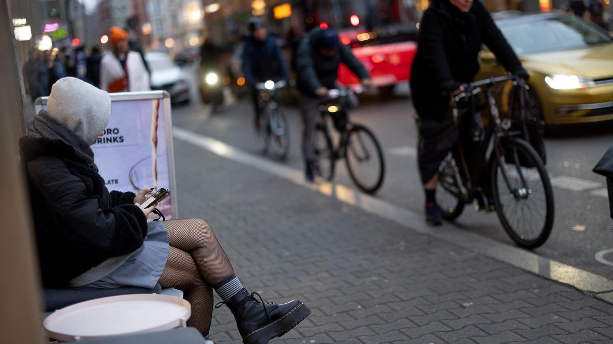 A person sits outside a coffee shop as cyclists and cars make their way on Scheunenviertel quarter in Berlin, Germany, November 15, 2024. REUTERS/Lisi Niesner