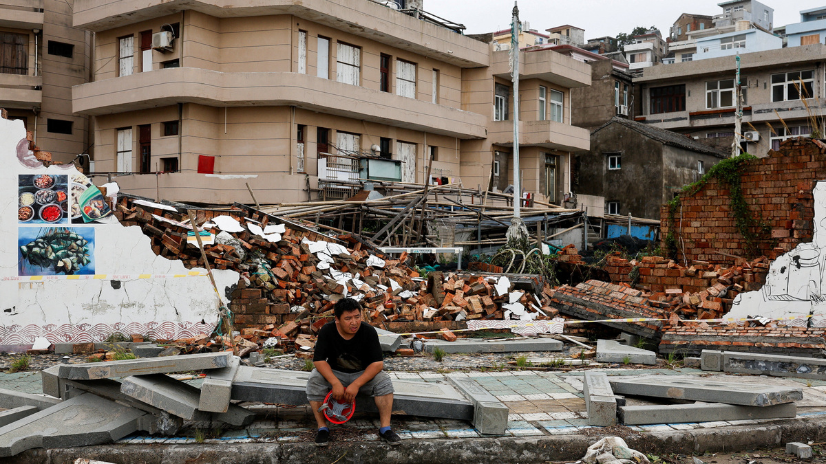 A person sits beside a collapsed wall in the aftermath of Typhoon Bavi in the coastal village of Dongsha, Taizhou, Zhejiang province, China, July 12, 2026. REUTERS/Go Nakamura