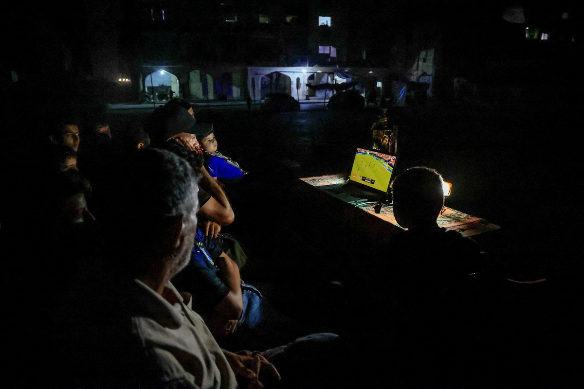 Former Palestinian soccer player Fadi Al-Arawi watches a 2026 World Cup match streamed on a laptop alongside others in Khan Younis, in the southern Gaza Strip, June 13, 2026. REUTERS/Haseeb Alwazeer