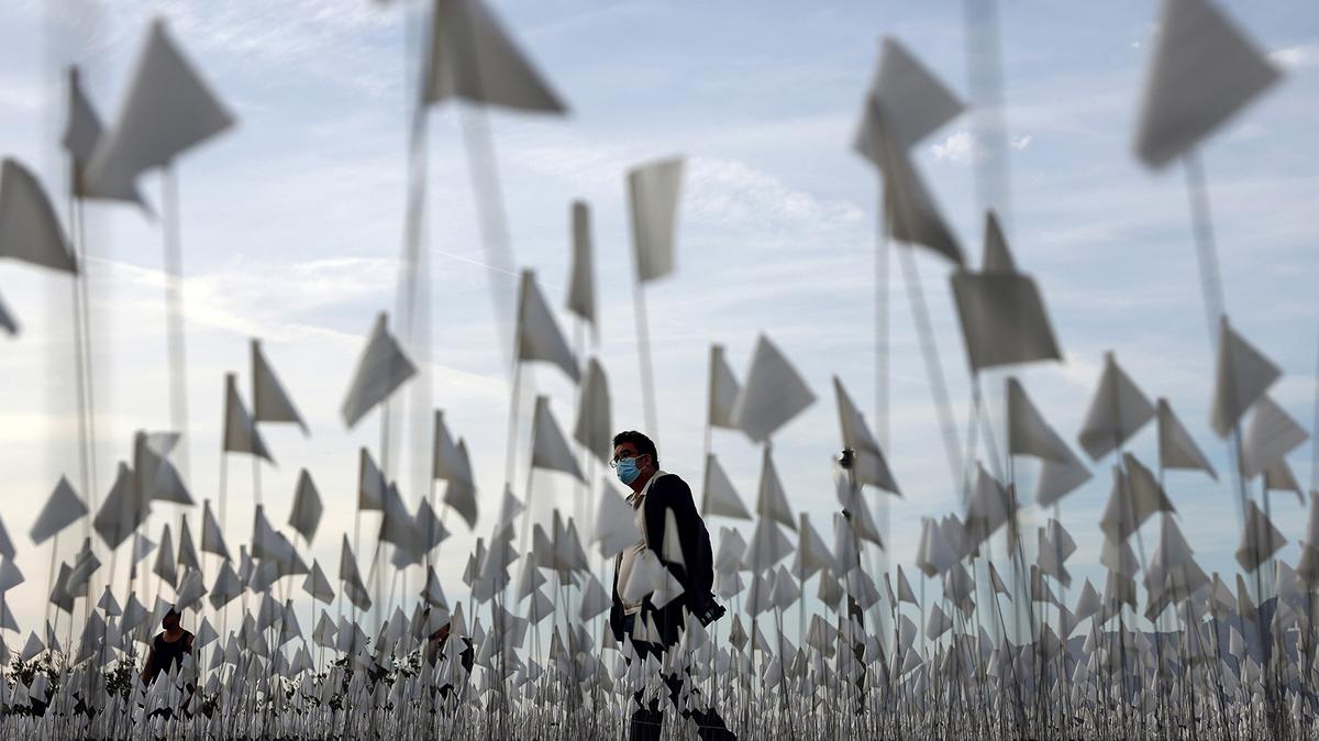 A person wearing a face covering walks past a white flag memorial installation outside Griffith Observatory honoring the nearly 27,000 Los Angeles County residents who have died from COVID-19 on Nov. 18, 2021, in Los Angeles, California. (Mario Tama/Getty Images/TNS)