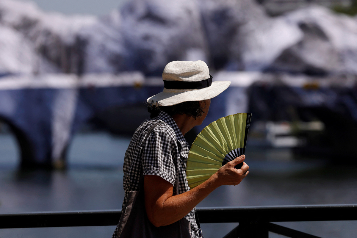 A person wearing a hat and holding a hand fan walks on the Pont des Arts bridge over the River Seine in Paris as temperatures rise during a heatwave affecting a large part of France, June 22, 2026. REUTERS/Alice Sacco