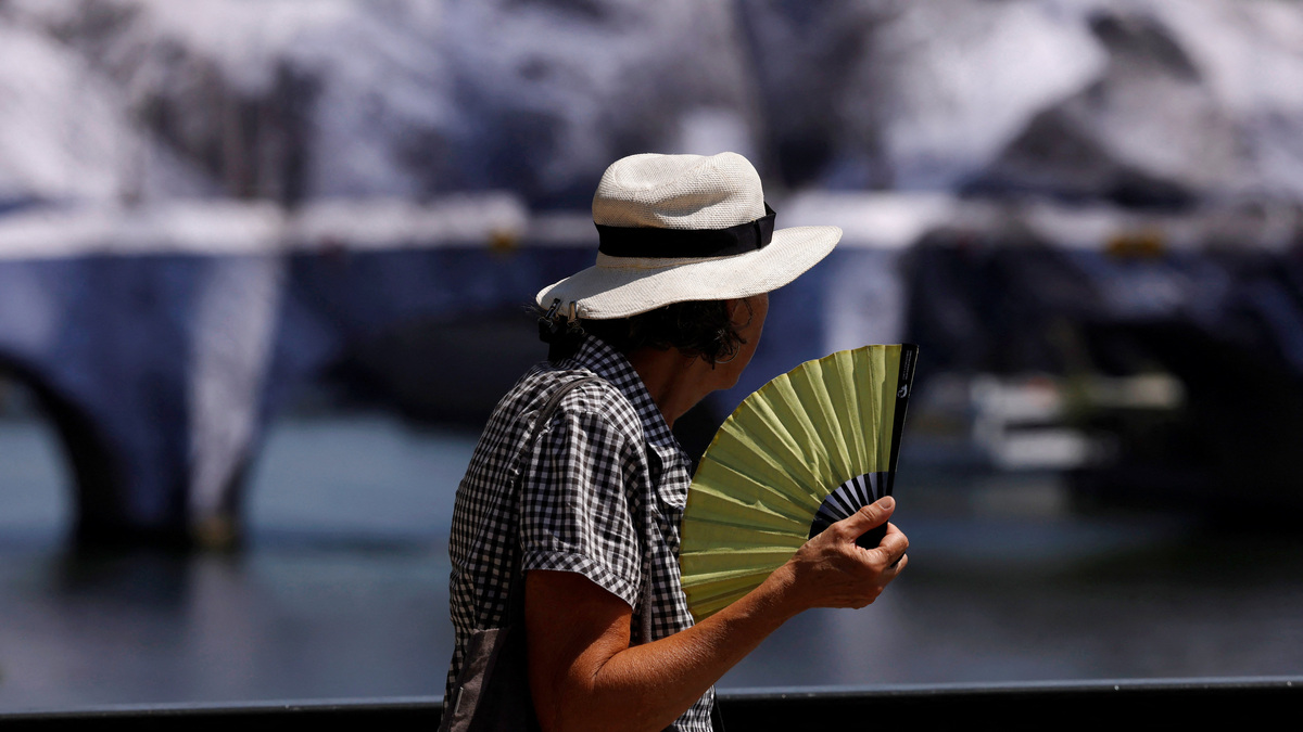 A person wearing a hat and holding a hand fan walks on the Pont des Arts bridge over the River Seine in Paris as temperatures rise during a heatwave affecting a large part of France, June 22, 2026. REUTERS/Alice Sacco