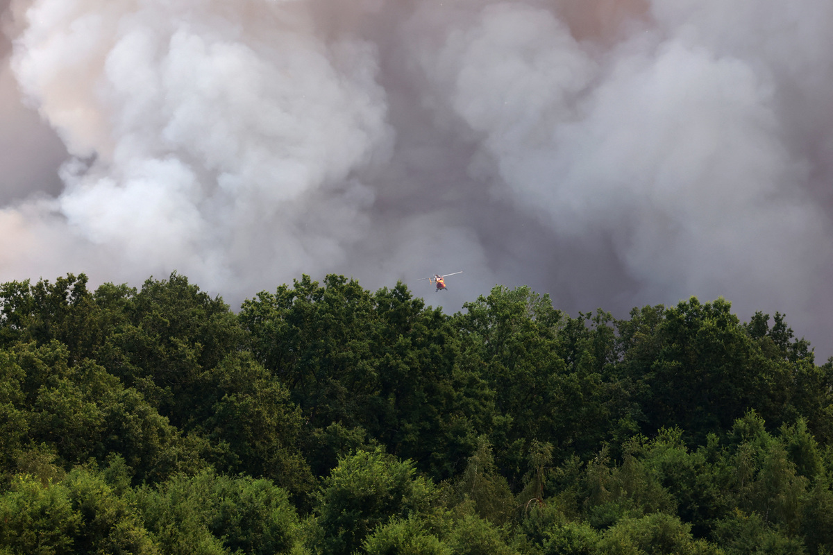 A firefighting helicopter flies through plumes of smoke above the Fontainebleau forest as a wildfire burns near Paris during a heatwave affecting large parts of France, July 13, 2026. REUTERS/Stephane Mahe