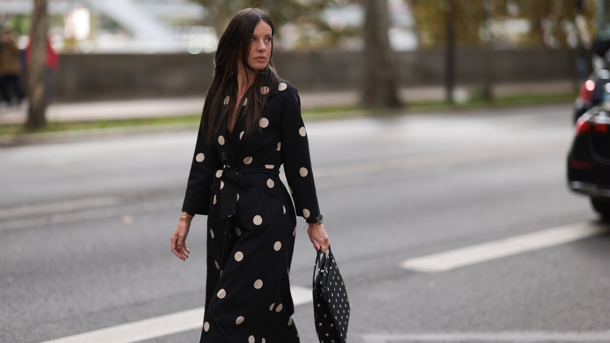 PARIS, FRANCE - SEPTEMBER 28: A Fashion Week guest is seen wearing round diamond stud earrings; a long-sleeved black midi dress with white polka dot pattern, notched lapels, and a tie belt; a gold bangle; a rose gold and black watch from Rolex; a gold ring; and a rectangular black handbag with a white polka dot pattern before the Elie Saab Womenswear Spring/Summer 2025 Show as part of Paris Fashion Week on September 28, 2024 in Paris, France. (Photo by Jeremy Moeller/Getty Images)