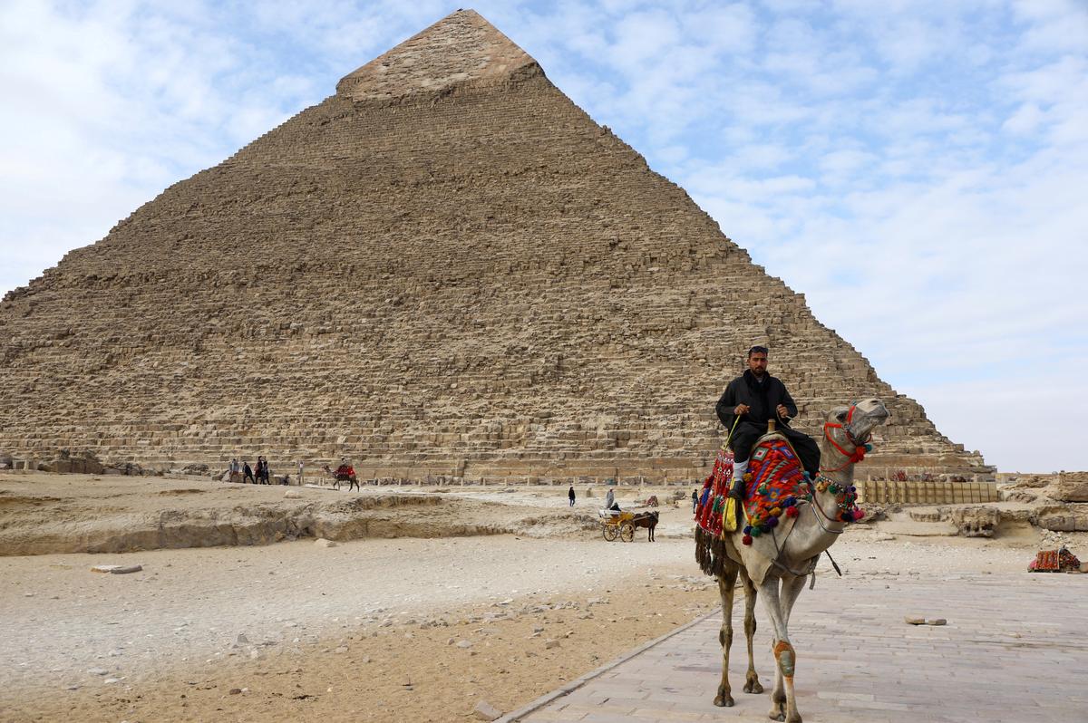 FILE PHOTO: A man waits for tourists to rent his camel in front of the Pyramid of Khufu, the largest of the Great Pyramids of Giza, on the outskirts of Cairo, Egypt January 18, 2020. REUTERS/Marius Bosch/File Photo