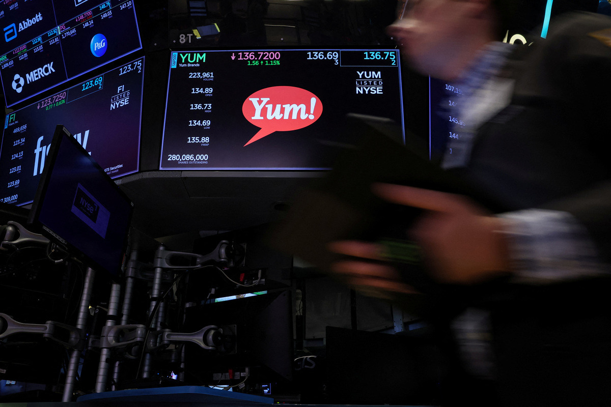 The Yum brand logo and trading information are displayed on a screen as a trader passes by on the floor of the New York Stock Exchange (NYSE) in New York City, U.S., June 29, 2023.  REUTERS/Brendan McDermid