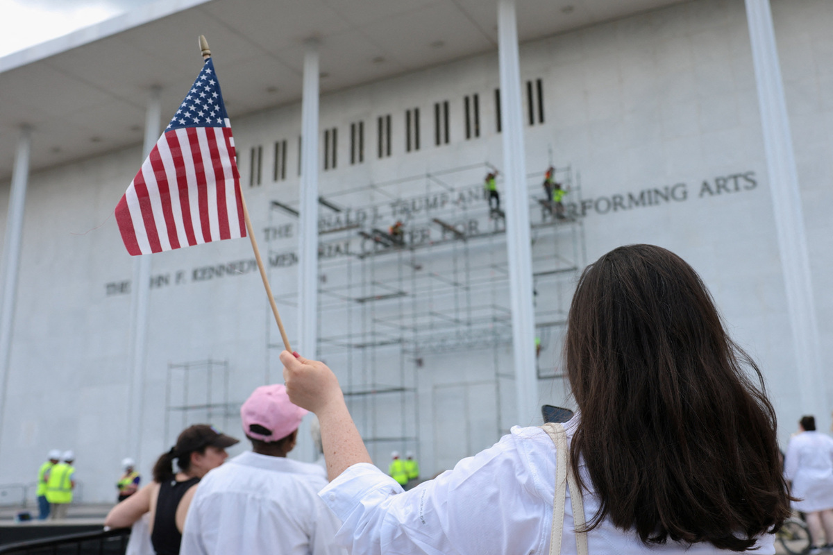 A person waves an American flag as workers set up scaffolding to remove lettering from the facade of the John F. Kennedy Memorial Center for the Performing Arts, following a federal judge’s order to remove U.S. President Donald Trump's name from the institution, in Washington, D.C., U.S., June 12, 2026. REUTERS/Jonathan Ernst