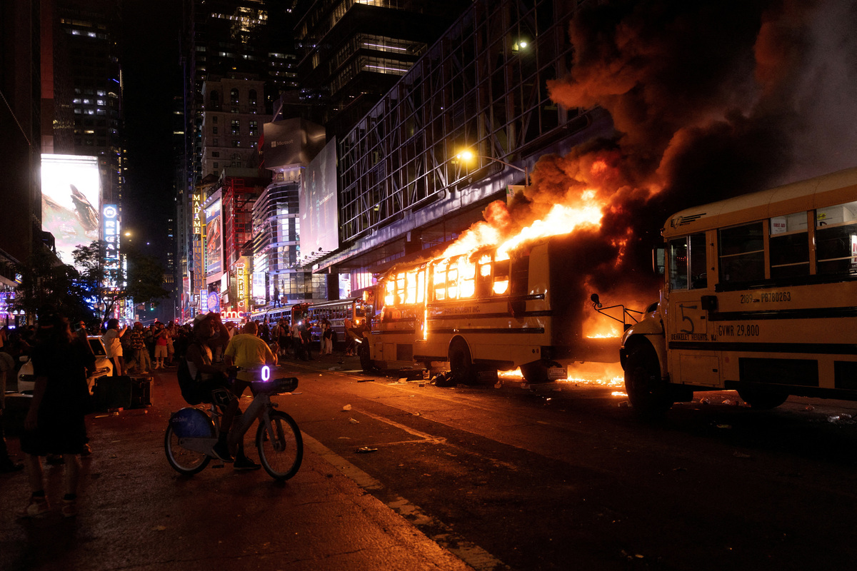 Revellers and fans celebrating the New York Knicks' win over the San Antonio Spurs and World Cup festivities watch as a city shuttle bus catches fire outside the Port Authority Bus Terminal in New York, U.S., June 14, 2026. The shuttles had been brought in to transport spectators to and from the New York/New Jersey stadium for the 2026 FIFA World Cup. REUTERS/Ed Ou