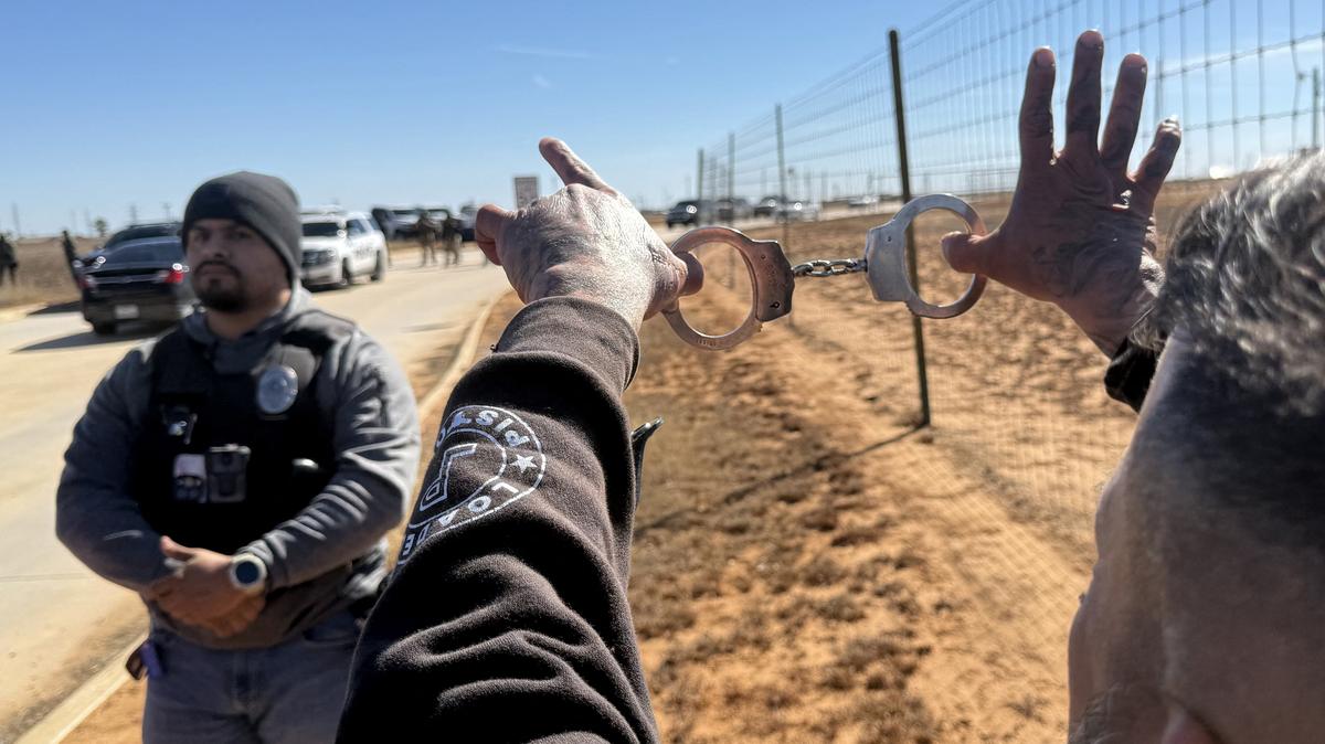 A protestor holds up a pair of handcuffs in front of a law enforcement officer as people gather during a demonstration and vigil outside the South Texas Family Residential Center in Dilley, Texas, on Jan. 28, 2026. Five-year-old Liam Conejo Ramos and his father, Adrian Conejo Arias, asylum seekers from Ecuador who were arrested on January 20 in Minneapolis by ICE agents, are being held at the center along with others detained by ICE. US President Donald Trump said on January 27 that he would "de-escalate a little bit" in Minneapolis after the fatal shootings of two civilians fueled a storm of criticism over his signature immigration crackdown. (Moisés Avila/AFP/Getty Images/TNS)