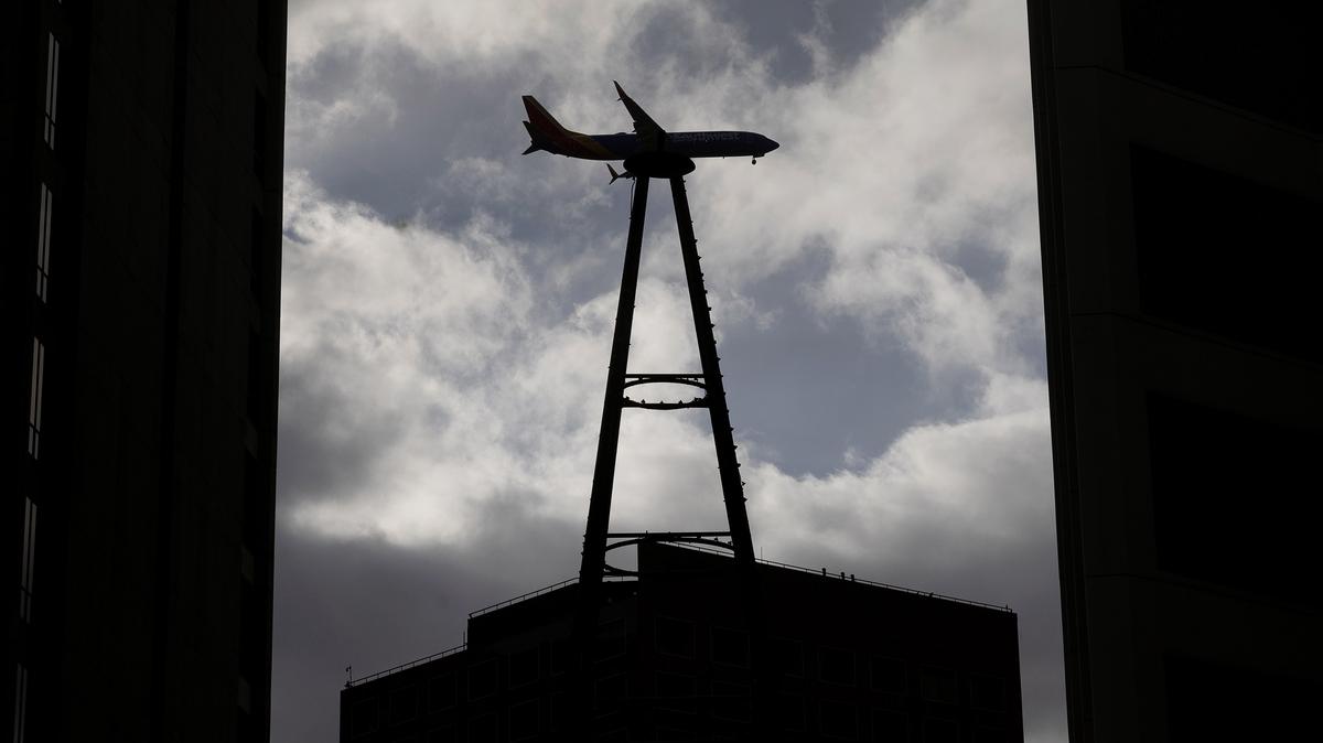A jet headed to San Jose Mineta International Airport passes behind the scale model replica of the San Jose Electric Light Tower in Plaza de Cesar Chavez, Friday, Dec. 27, 2024.  (Karl Mondon/Bay Area News Group)