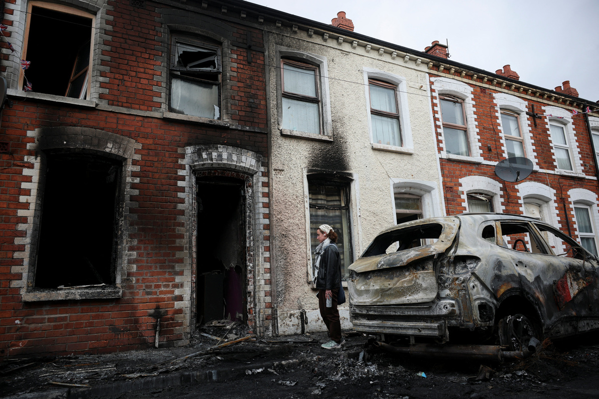 A resident looks at the charred debris scattered on the street in her neighbourhood, in the aftermath of anti-immigrant protests following a knife attack on June 8, which left a man seriously injured and prompted police to declare a critical incident, at Lendrick street, east Belfast, Northern Ireland, June 10, 2026. REUTERS/Isabel Infantes