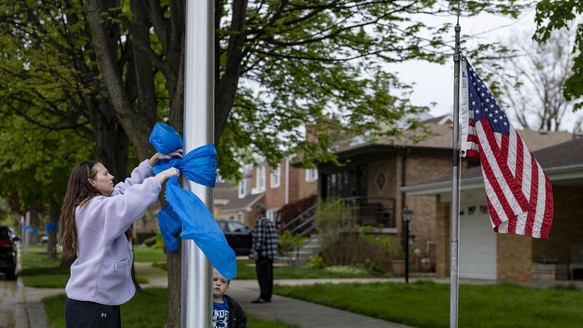Nora Draniczarek and her son Joe, 3, tie blue ribbons down the block, April 26, 2026, in the Edison Park neighborhood of Chicago for a neighbor, Chicago police Officer John Bartholomew, who was shot and killed Saturday at Endeavor Health Swedish Hospital. (Brian Cassella/Chicago Tribune/TNS)