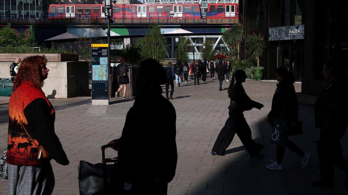 People walk in the financial and business district of Canary Wharf as a Docklands Light Railway train passes by, in London, Britain, April 13, 2026.  REUTERS/Kevin Coombs