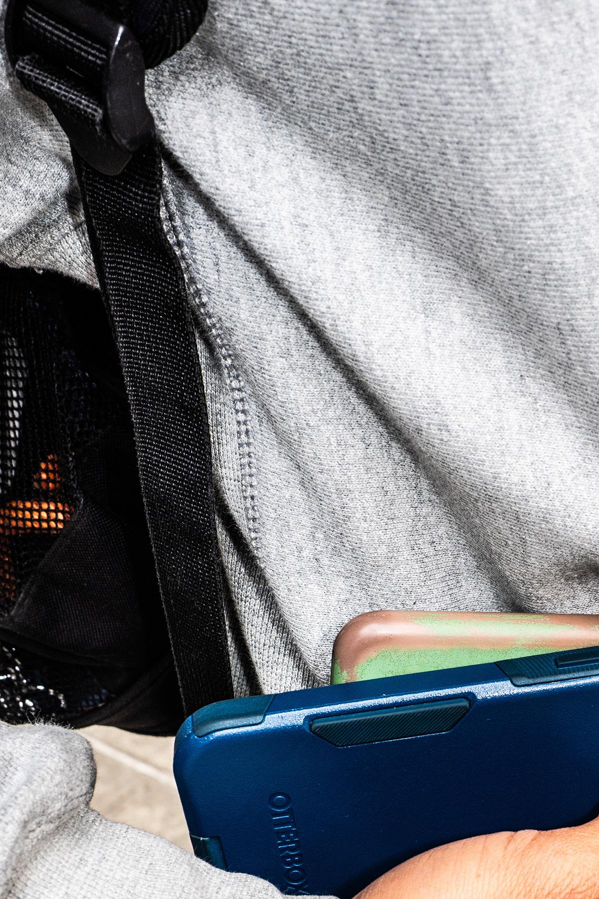 Rockie Cedeno, who runs Doors & Dawgs, a dog-walking business, puts two phones into the front pouch of his hoodie in New York, May 11, 2026. For him, pants are off-limits when it comes to phone storage. (Graham Dickie/The New York Times)