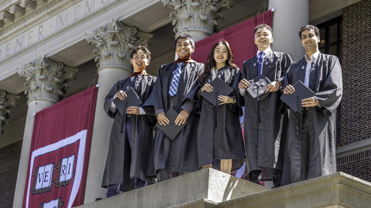 Five Harvard Students Smiling at Graduation Widner Library Cambridge MA. Five graduating students at Harvard University personify “higher education” as they pose for a picture standing at the top of the parapet wall at Widener Library. 

In the background hang huge “Veritas” banners with the Harvard’s logo.