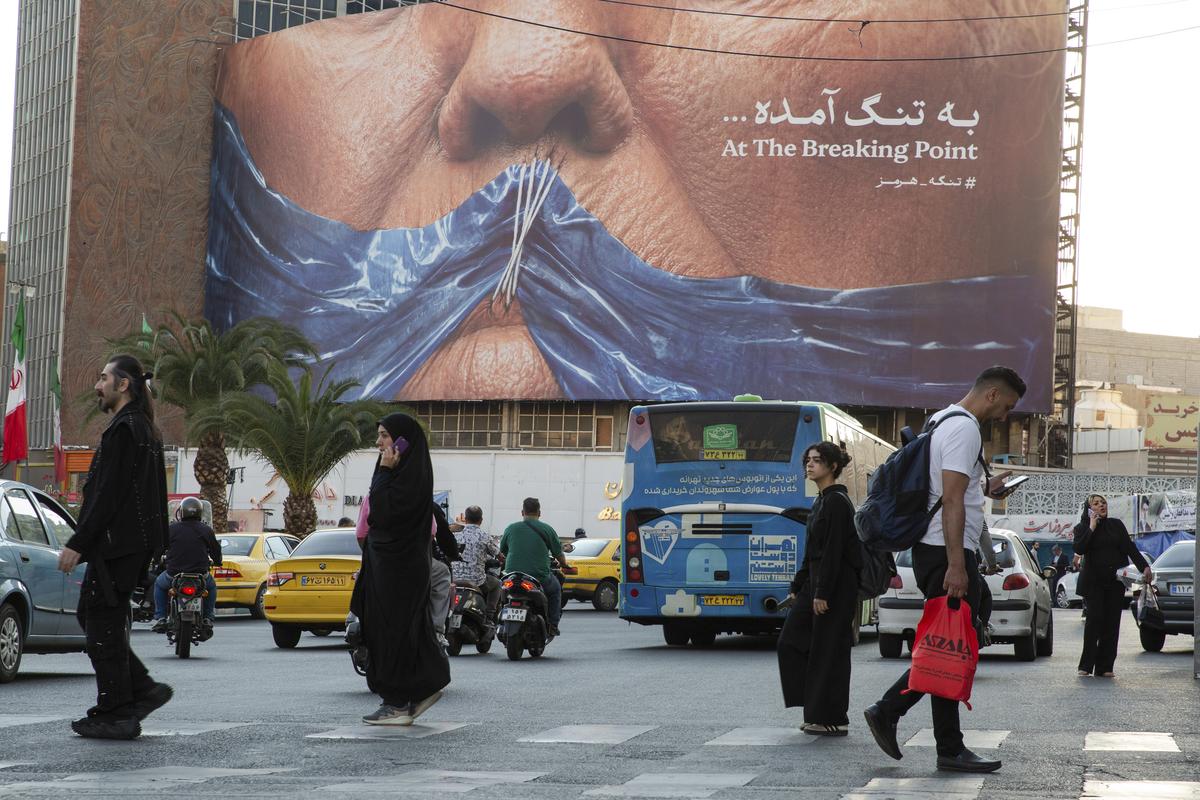 FILE -- People pass near a billboard showing the closure of the Strait of Hormuz over President Donald Trump's face with a message reading "At the Breaking Point" in Tehran, May 2, 2026. Beijing has strong strategic reasons to avoid siding explicitly with the United States and Israel against Iran, its partner in the Middle East, in a war it has repeatedly said should not have happened. (Arash Khamooshi/The New York Times)